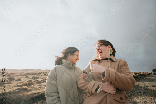 Two young women, on winter cloths during a windy day, enjoying a day while having fun running togueter between electric windmill . Lifestyle. Hipster and modern style. Cinema style. photo