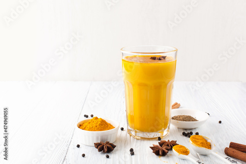 Golden turmeric latte in glass, spices and cinnamon on white wooden background.
