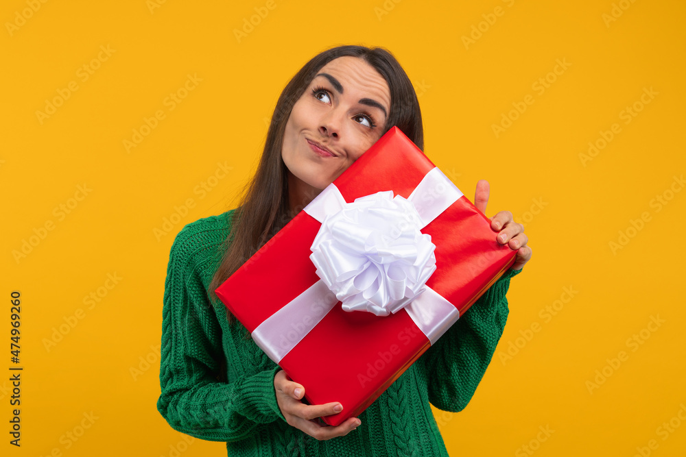Portrait of a cute girl holding a big decorated gift box in hands curious about what's inside, isolated over bright colored yellow background Portrait of a cute girl holding a big decorated gift box in hands curious about what's inside, isolated over bright colored yellow background