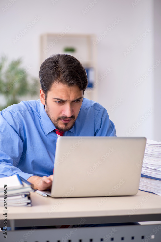 Young male employee unhappy with excessive work in the office Young male employee unhappy with excessive work in the office