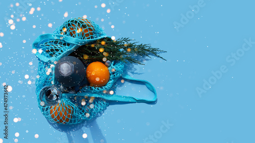 Christmas and New Year Composition. Blue String bag with champagne, oranges and branch of fir. Reusable shopping bag. Eco friendly mesh bags.