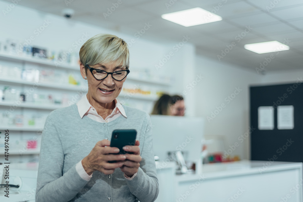 Smiling senior female patient in a pharmacy using smartphone Smiling senior female patient in a pharmacy using smartphone