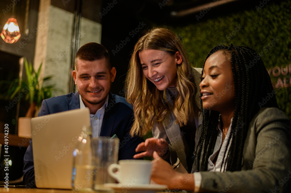 Cheerful work colleagues working on a laptop while having a meeting in a cafe Cheerful work colleagues working on a laptop while having a meeting in a cafe