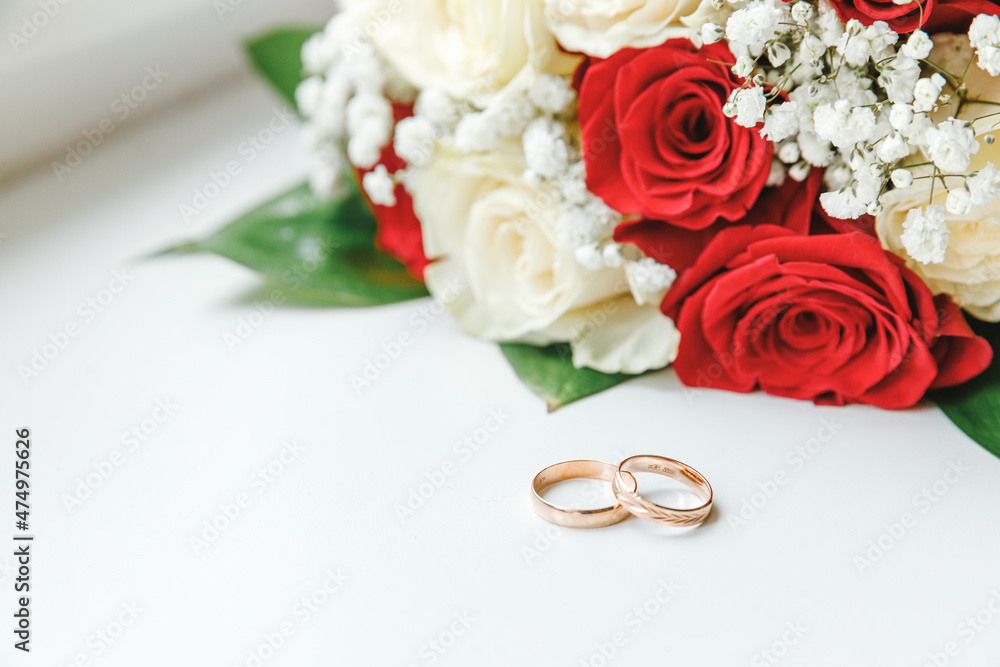 Gold wedding rings and flowers bouquet in white red colors lying on white background. Declaration of love, spring. Wedding card, Valentine's Day greeting. Wedding rings. Wedding day details Gold wedding rings and flowers bouquet in white red colors lying on white background. Declaration of love, spring. Wedding card, Valentine's Day greeting. Wedding rings. Wedding day details