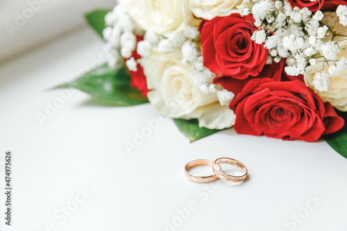 Gold wedding rings and flowers bouquet in white red colors lying on white background. Declaration of love, spring. Wedding card, Valentine's Day greeting. Wedding rings. Wedding day details