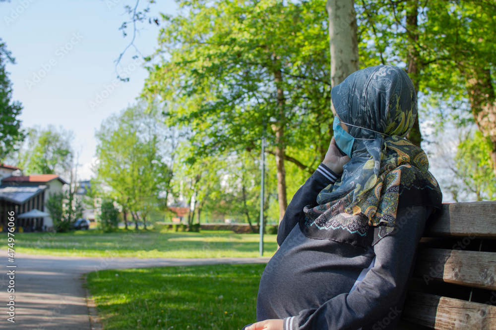 Profile view of the muslim pregnant woman wearing face mask talking on the smarphone