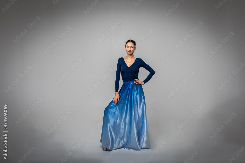 Beautiful ballerina stands looking straight into the camera in a long blue dress on a light background Beautiful ballerina stands looking straight into the camera in a long blue dress on a light background