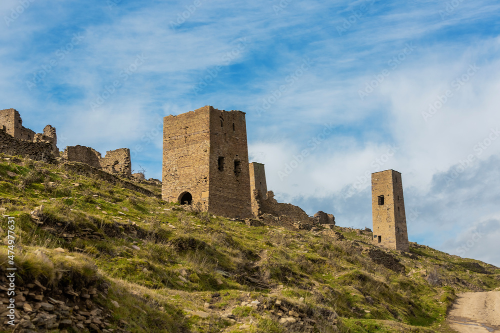 Ruins and towers of the abandoned village of Goor, Dagestan, Russia. Stone towers on the background of blue sky on the emerald hills. Panoramic view of the ancient Goor settlement among the mountains
