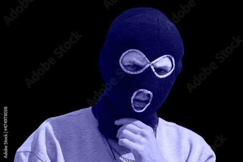 Closeup headshot of criminal wearing very pery balaclava and hoodie looking at camera, copy space, isolated over black background. very peri colored. Color of the year 2022 photo