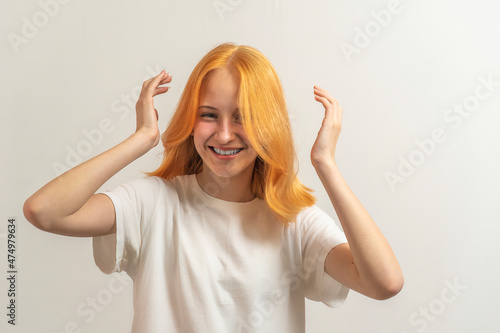 teen girl with red hair in a white t-shirt on a light background laugh and straighten hair
