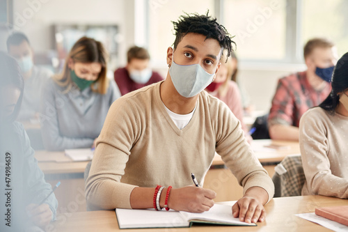 Black male student wears face mask while writing notes during lecture at the university.
