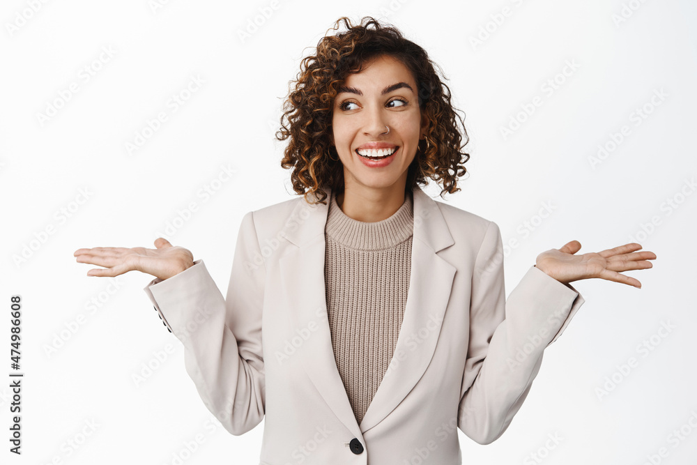Image of cute corporate woman, office lady shrugging shoulders and smiling, looking unaware, clueless, dont care, standing in suit over white background Image of cute corporate woman, office lady shrugging shoulders and smiling, looking unaware, clueless, dont care, standing in suit over white background