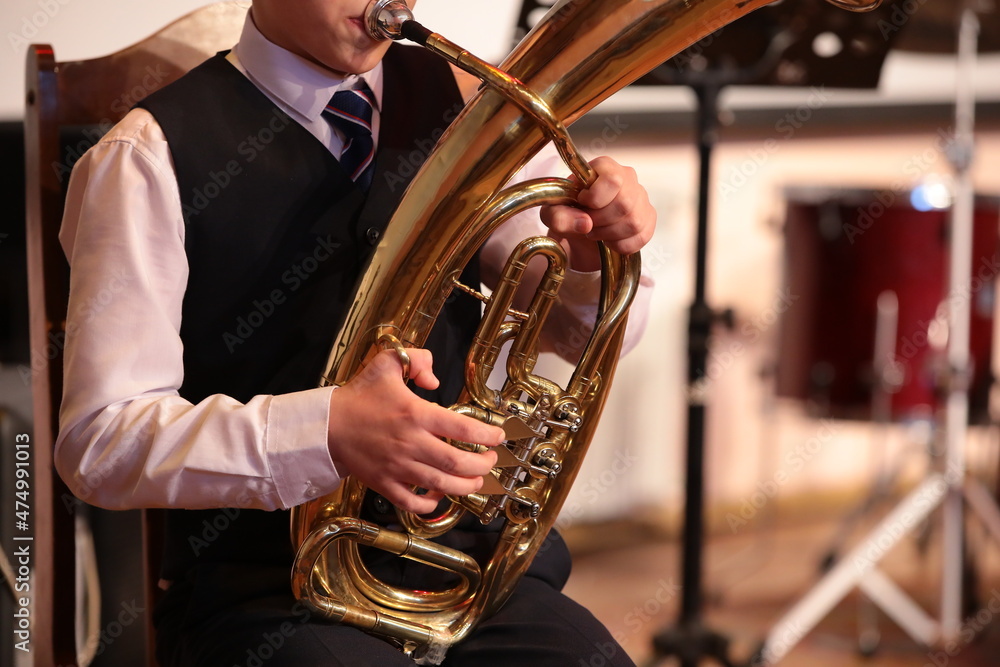 Obraz premium Young man playing a tuba on a golden big trumpet sitting on a chair blowing a mouthpiece holding hand equipment musician frontal close-up portrait