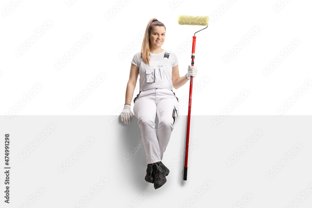 Full length portrait of a female house painter sitting on a blank panel with a paint roller Full length portrait of a female house painter sitting on a blank panel with a paint roller