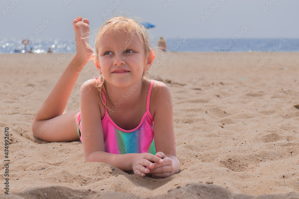 little girl, blonde, 6 years old, lies in a bright bikini on the sand