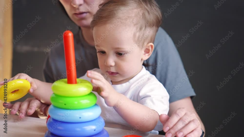 baby collects toy pyramid. mom plays with her son at home happy family. development of fine motor skills in newborn child. happy family mom and preschool baby play pyramid toy. kindergarten education