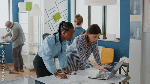 Team of diverse women using laptop to design blueprints plans for building construction on table. Expert architects working together with computer to plan urban development project.