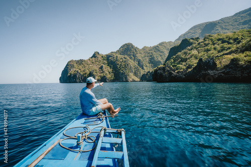 Back view of the man on boat with spreading hands arriving to exotic tropical island lit by sun light. Travelling tour in Asia: El Nido, Palawan, Philippines