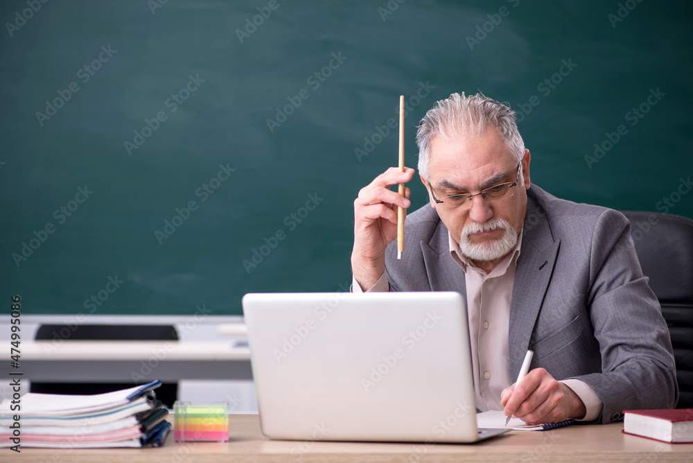 Old male teacher in front of blackboard Old male teacher in front of blackboard