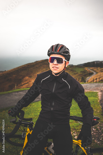 Young caucasian cyclist man standing on his bike at the top of a climb. © Jorge Argazkiak