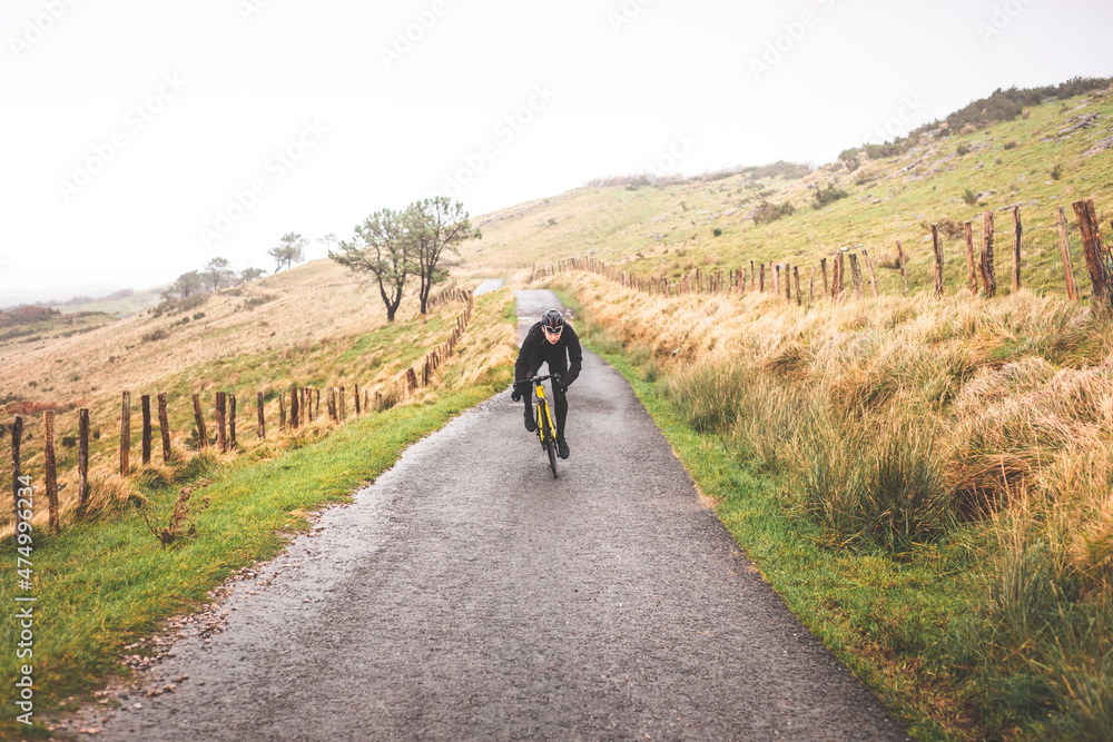 Young caucasian cyclist man sprinting while climbing a hill in a foggy mountain.