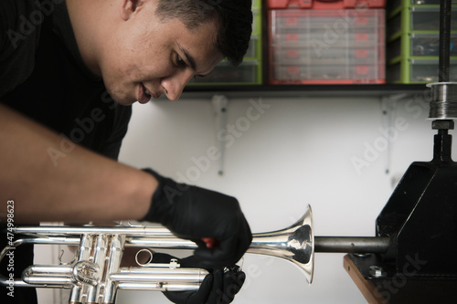 Latin male instrument repairer disassembling a trumpet in his repair shop photo