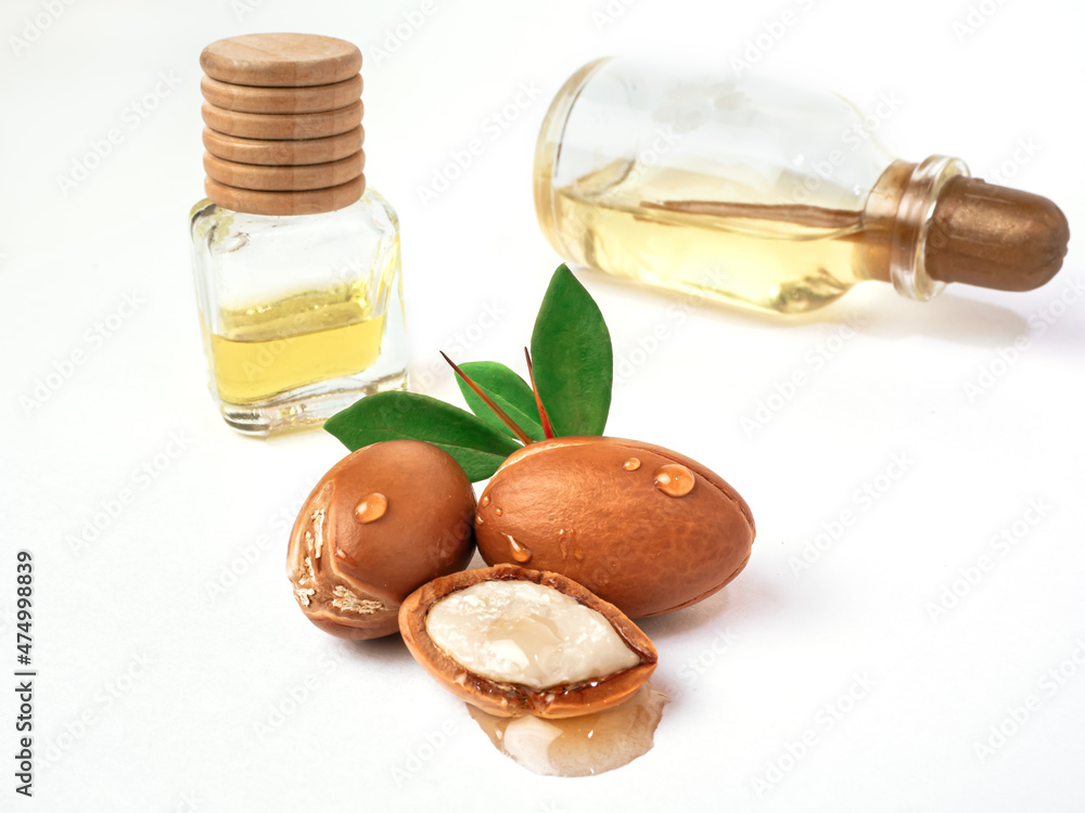 Three argan nuts with green leaves glass bottles on isolated white