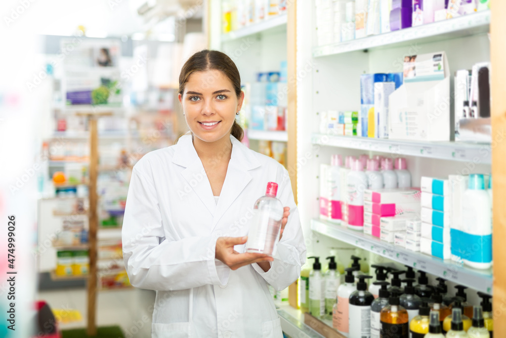Portrait of a smiling young female pharmacist in the sales hall of a pharmacy, demonstrating recently received goods for .sale in hands