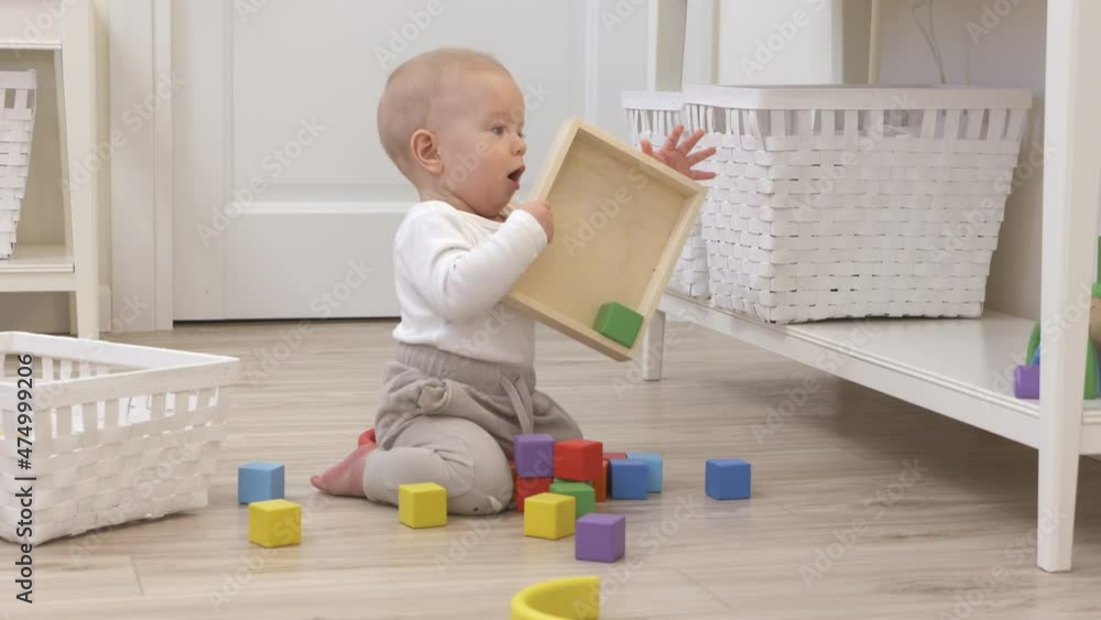 Baby boy sitting on the floor playing with wooden building blocks stacking game, cute 9 month old toddler picks up and examines rainbow cubes at home. High quality 4k footage Baby boy sitting on the floor playing with wooden building blocks stacking game, cute 9 month old toddler picks up and examines rainbow cubes at home. High quality 4k footage