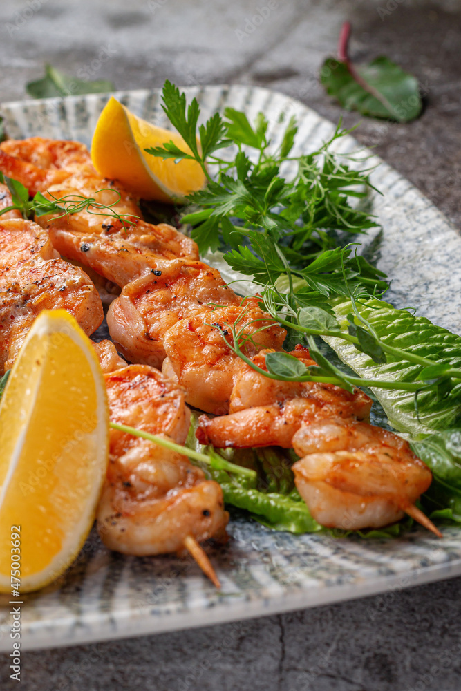 Grilled king prawns with lemon and herbs on a plate against a gray stone table, fish kebab Grilled king prawns with lemon and herbs on a plate against a gray stone table, fish kebab