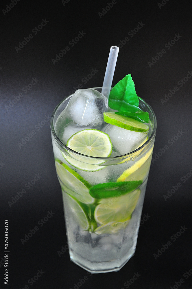 Tall glass of refreshing Mojito with ice, mint and lime slices on a black background. Tall glass of refreshing Mojito with ice, mint and lime slices on a black background.