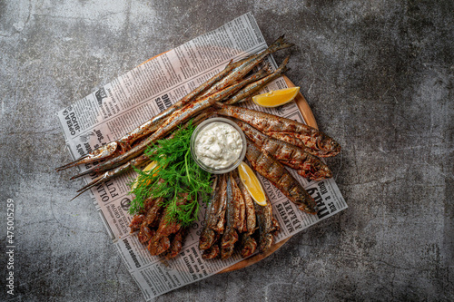 An fish appetizer in a restaurant, fried sprat on a wooden plate with lemon and cream sauce against a gray stone table  photo