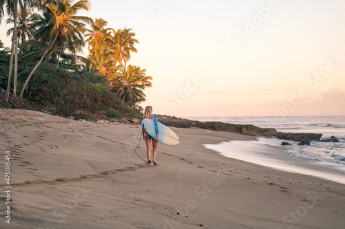 Portrait of blond surfer girl with white surf board in blue ocean pictured from the water in Encuentro beach