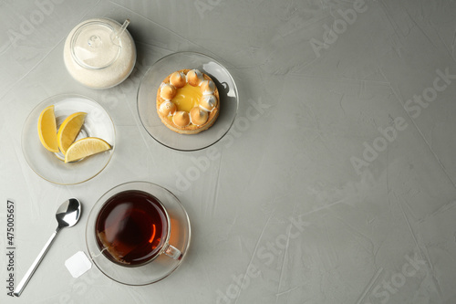 Flat lay composition with tea bag in ceramic cup of hot water and dessert on grey table. Space for text