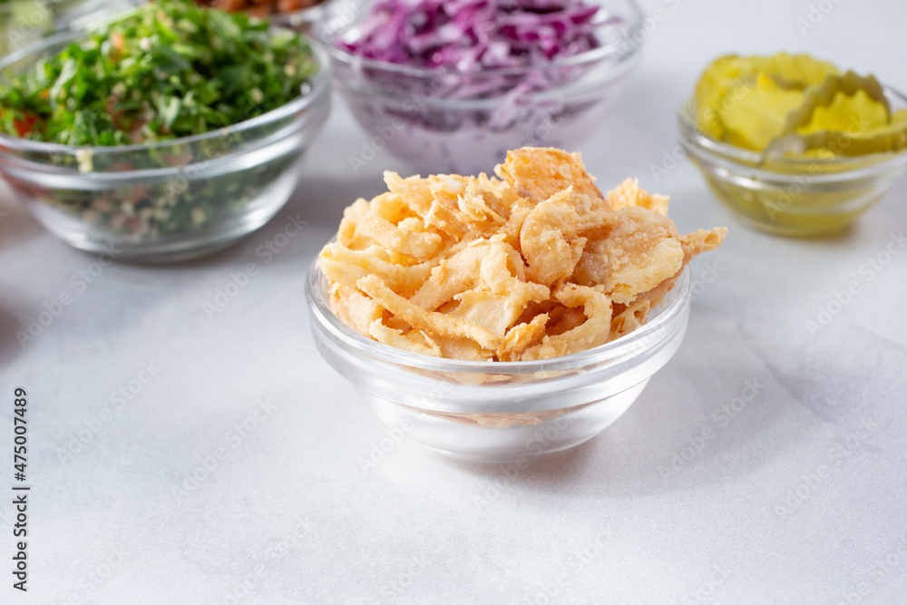 A view of a glass condiment cup of deep fried onions or fried tortilla strips, among a variety of other chopped ingredients. A view of a glass condiment cup of deep fried onions or fried tortilla strips, among a variety of other chopped ingredients.