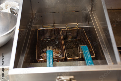 A view of deep fryer baskets boiling in hot oil, in a restaurant kitchen setting.
