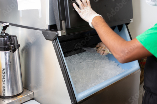 A view of an employee scooping ice out of an ice machine, in a restaurant setting.