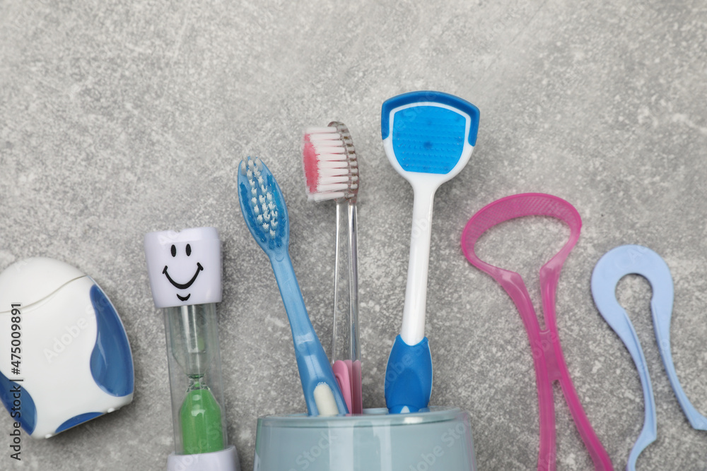 Tongue cleaners, toothbrushes, dental floss and hourglass on light grey background, flat lay Tongue cleaners, toothbrushes, dental floss and hourglass on light grey background, flat lay
