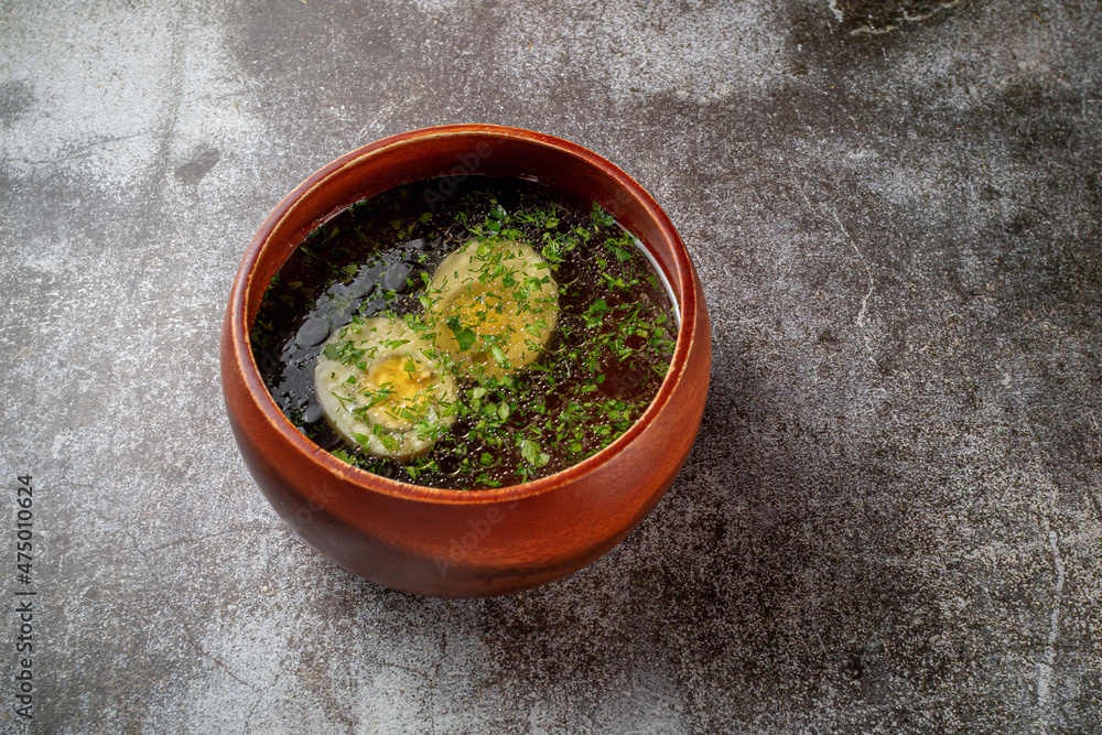 Chicken soup with boiled egg sprinkled with dill and parsley greens in a wooden bowl with bread crumbs stands isolated on a stone table, Flatlay Chicken soup with boiled egg sprinkled with dill and parsley greens in a wooden bowl with bread crumbs stands isolated on a stone table, Flatlay