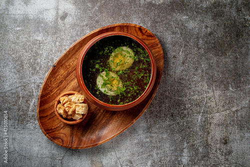 Chicken soup with boiled egg sprinkled with dill and parsley greens in a wooden bowl with bread crumbs stands isolated on a stone table, Flatlay
