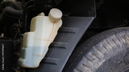 Truck coolant tank. The white plastic tank has coolant in the engine radiator system on a dark background and rubber wheels with copy space. Auto parts concept. Closeup and focus on the subject. photo