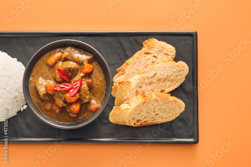 Bowl with tasty beef curry  bread and rice on color background