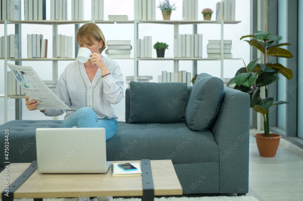 Happy Caucasian senior woman is relaxing , reading newspaper in living room Happy Caucasian senior woman is relaxing , reading newspaper in living room