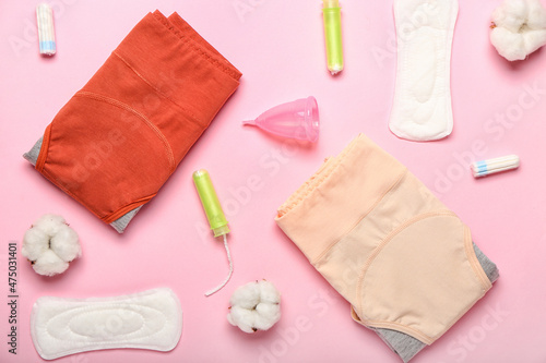 Composition with period panties, pads, tampons, menstrual cup and cotton flowers on pink background