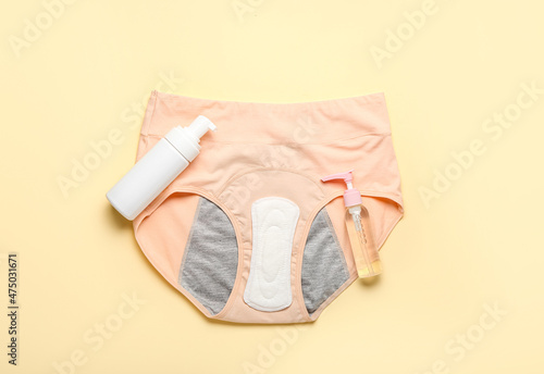 Period panties, pad and bottles of cosmetic products on color background