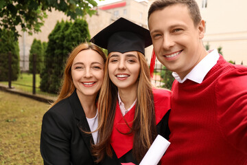 Happy young woman with her parents taking selfie on graduation day