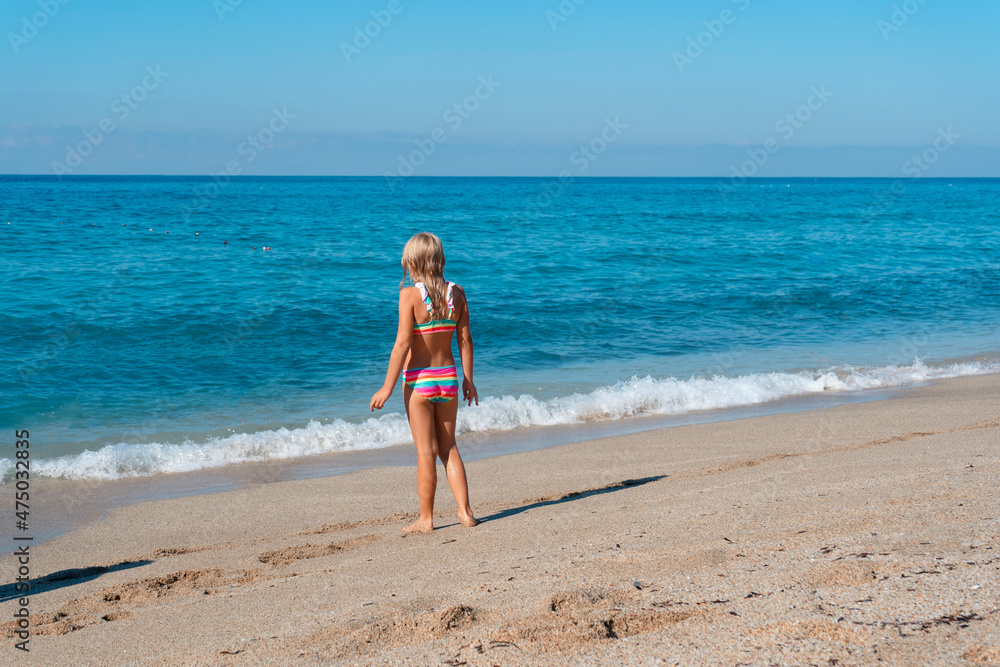 Blond preschool girl wearing colorful swimsuit near the sea on the sand beach on a beautiful summer sunny day. Blond preschool girl wearing colorful swimsuit near the sea on the sand beach on a beautiful summer sunny day.