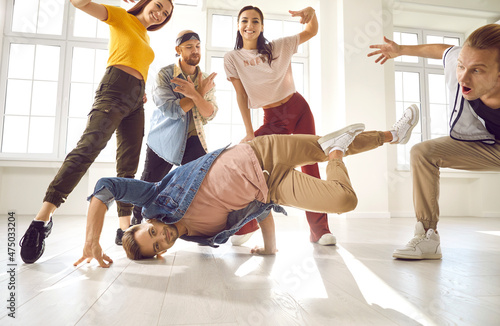 Talented youth. Young male dancer demonstrates his talent dancing breakdance in studio among other dancers. Group of positive people perform hip hop movements. Sport, dancing and urban culture concept photo