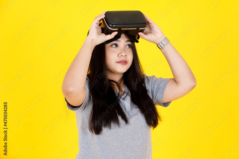 Portrait studio shot of Asian happy young chubby plump long black hair female gamer model in casual outfit smiling wearing big virtual reality vr camera goggles console game on yellow background Portrait studio shot of Asian happy young chubby plump long black hair female gamer model in casual outfit smiling wearing big virtual reality vr camera goggles console game on yellow background