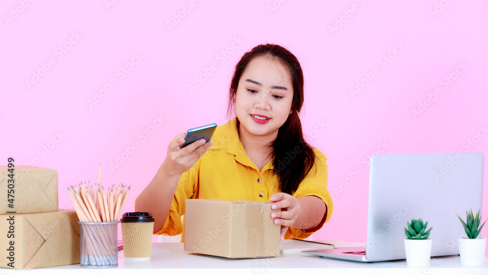 Studio shot of Asian young successful female startup entrepreneur businesswoman checking delivery shipping address for shipment package boxes from laptop computer on working desk on pink background Studio shot of Asian young successful female startup entrepreneur businesswoman checking delivery shipping address for shipment package boxes from laptop computer on working desk on pink background